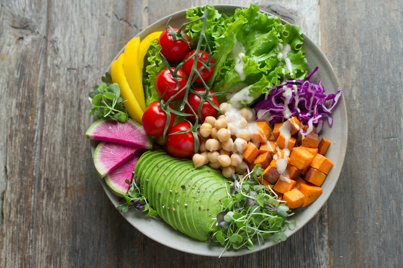 Overhead photograph of a vegetable bowl with greens, grains, seeds, and lemon